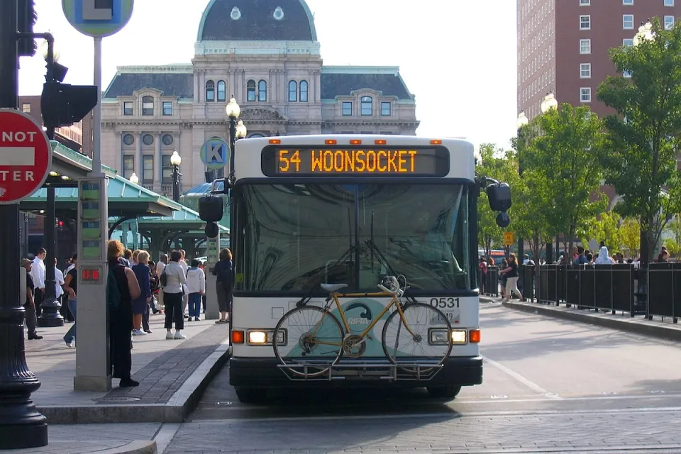 A white RIPTA bus with a bike on a front bike rack at a stop in Providence, Rhode Island.